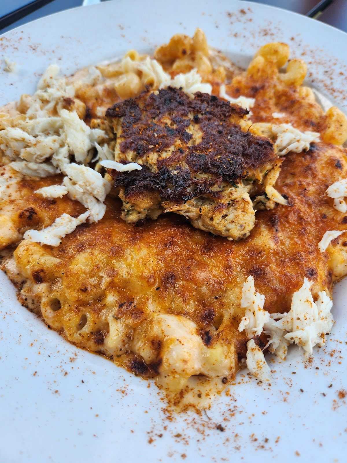 Creamy macaroni and cheese topped with a seasoned, grilled crab cake on a white plate.