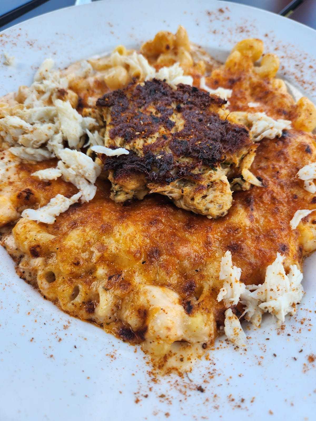 Creamy macaroni and cheese topped with a seasoned, grilled crab cake on a white plate.