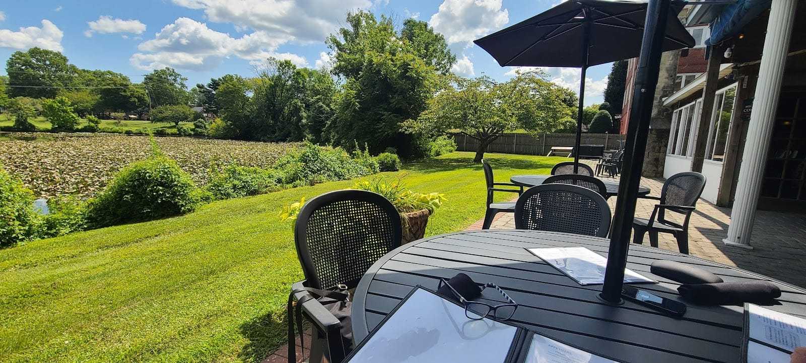 Outdoor patio with tables, chairs, and umbrellas overlooking a lush green landscape on a sunny day.
